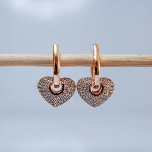Pair of gold heart earrings hanging on a stick, showcasing luxury jewelry design.