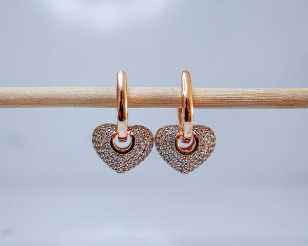 Pair of gold heart earrings hanging on a stick, showcasing luxury jewelry design.